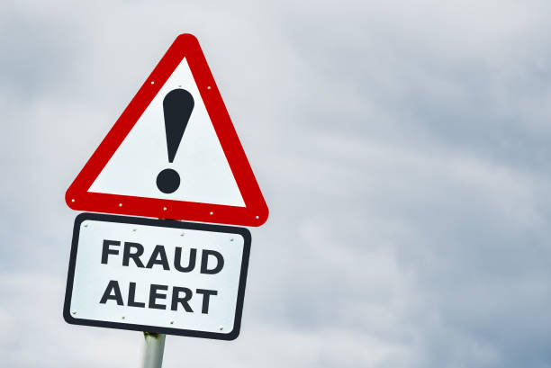 Conceptual triangular hazard road sign against a stormy sky saying fraud alert